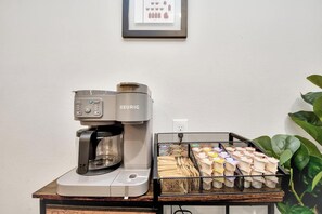 A Keurig coffee machine on a table with a basket of coffee pods and a tray of wooden spoons. - Modern Retreat l Sleeps 20+ l w/Loft Lounge (Houston)