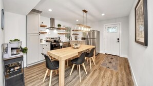 A modern kitchen with a wooden dining table, black chairs, a stainless steel refrigerator, and a hanging light fixture. - Modern Retreat l Sleeps 20+ l w/Loft Lounge (Houston)