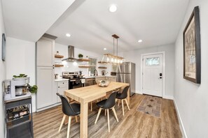 A modern kitchen with a wooden dining table, black chairs, a stainless steel refrigerator, and a hanging light fixture. - Modern Retreat l Sleeps 20+ l w/Loft Lounge (Houston)