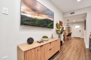 A modern interior with a wooden console, a large landscape painting, and a dining area with chairs and a table. - Modern Retreat l Sleeps 20+ l w/Loft Lounge (Houston)