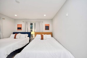 A hotel room with two beds, a window with curtains, a nightstand with a lamp, and a wall-mounted light fixture. - Modern Retreat l Sleeps 20+ l w/Loft Lounge (Houston)