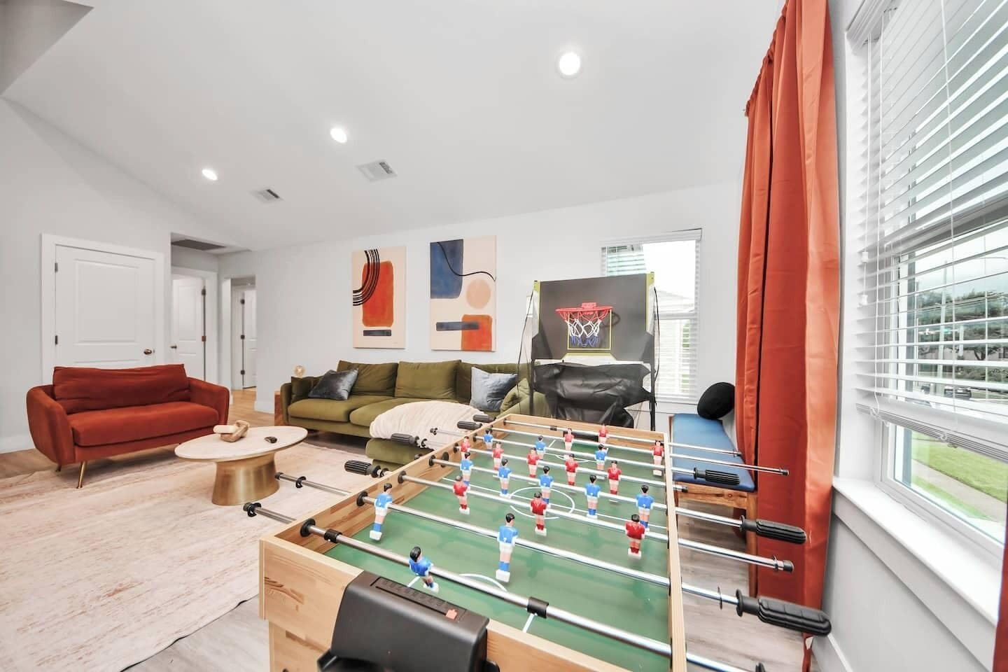 Ein Wohnzimmer mit einem Kicker, zwei Sofas, einem Couchtisch und einem fenster mit Vorhängen.
