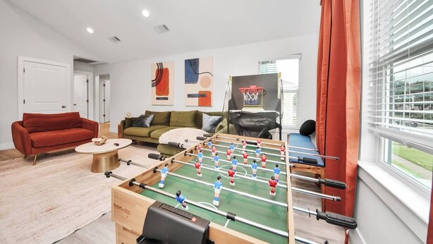 A living room with a foosball table, two sofas, a coffee table, and a window with curtains. - Modern Retreat l Sleeps 20+ l w/Loft Lounge (Houston)