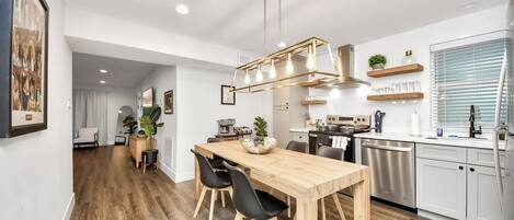 Una cocina moderna con una mesa de comedor de madera, sillas negras y una lámpara colgante.