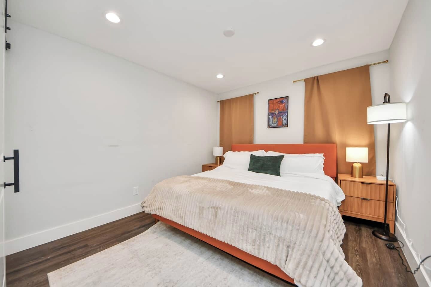 Ein Schlafzimmer mit einem Bett, Nachttischen, einer Lampe, einem Gemälde und Holzboden.