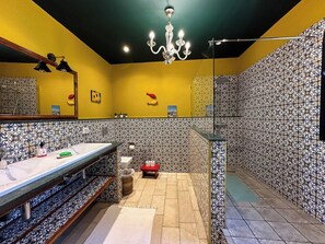 Une salle de bain avec un mur jaune, un pare-feu en carreaux noirs et blancs, un lavabo avec un miroir et un lustre.