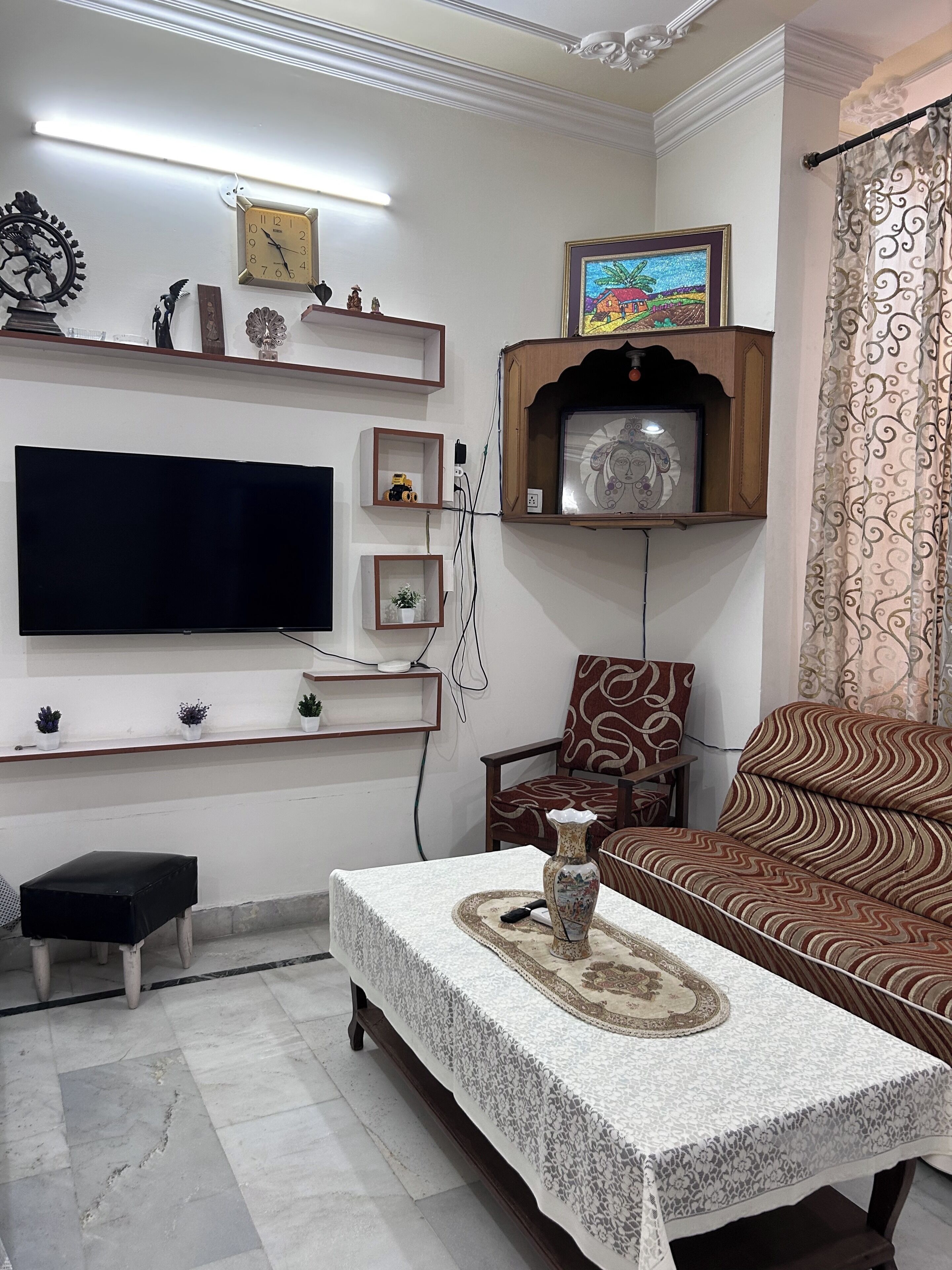 A living room with a flat-screen TV, a clock, a framed picture, a sofa, a coffee table, and a small bench.