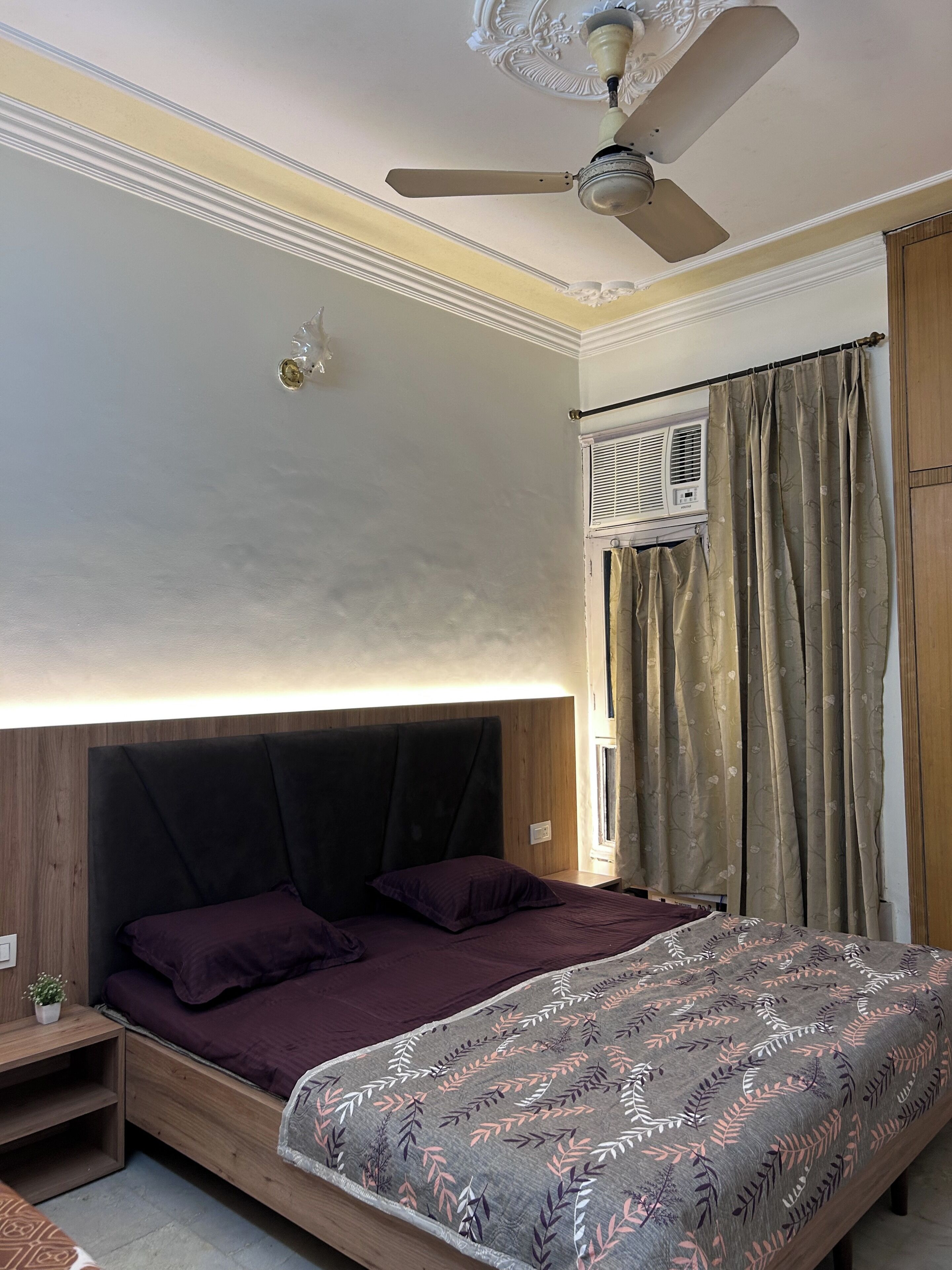 A bedroom with a bed, a ceiling fan, a window with curtains, and a wall-mounted air conditioner.