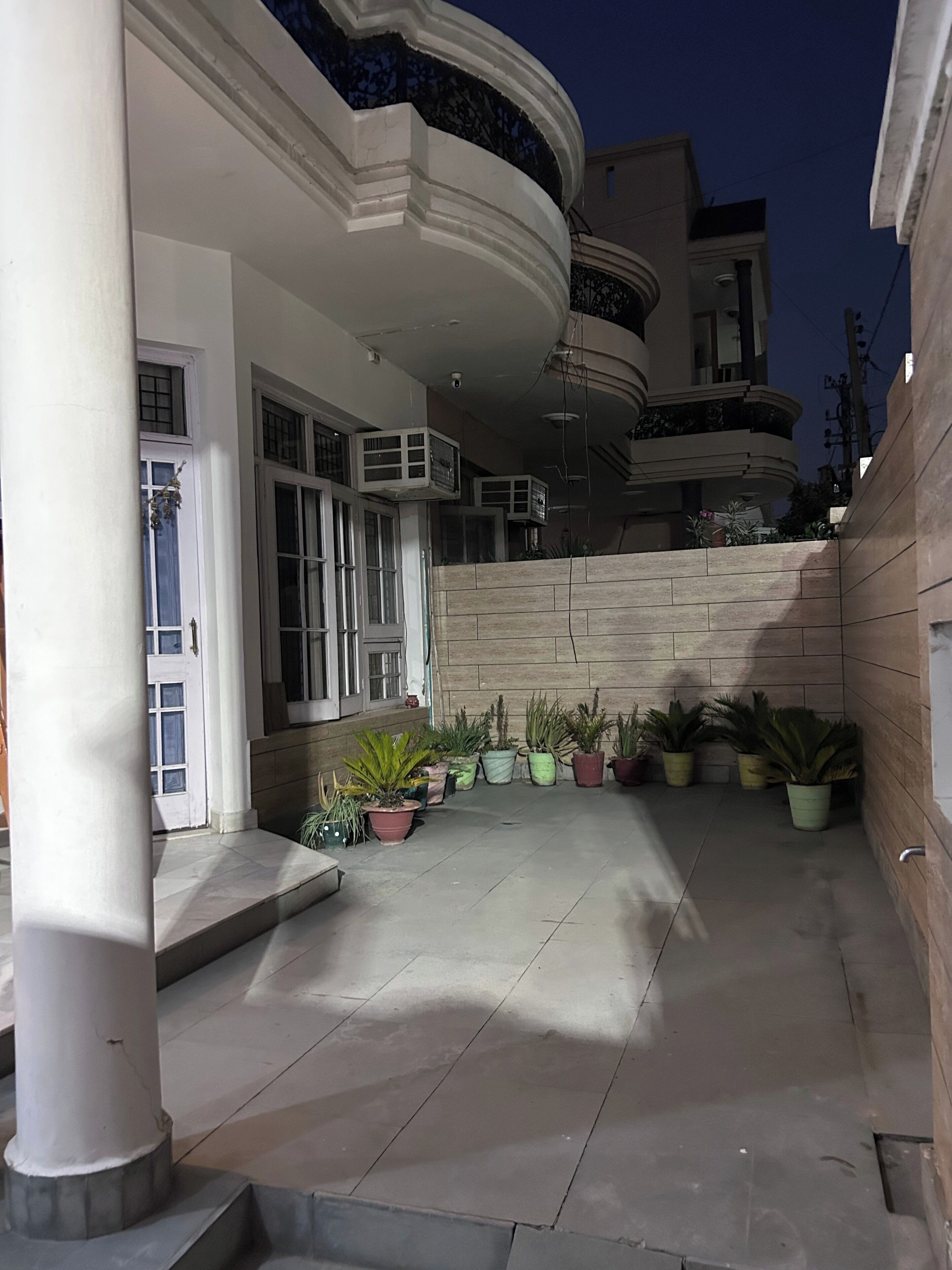 A building with a curved balcony, a stone wall, and potted plants.