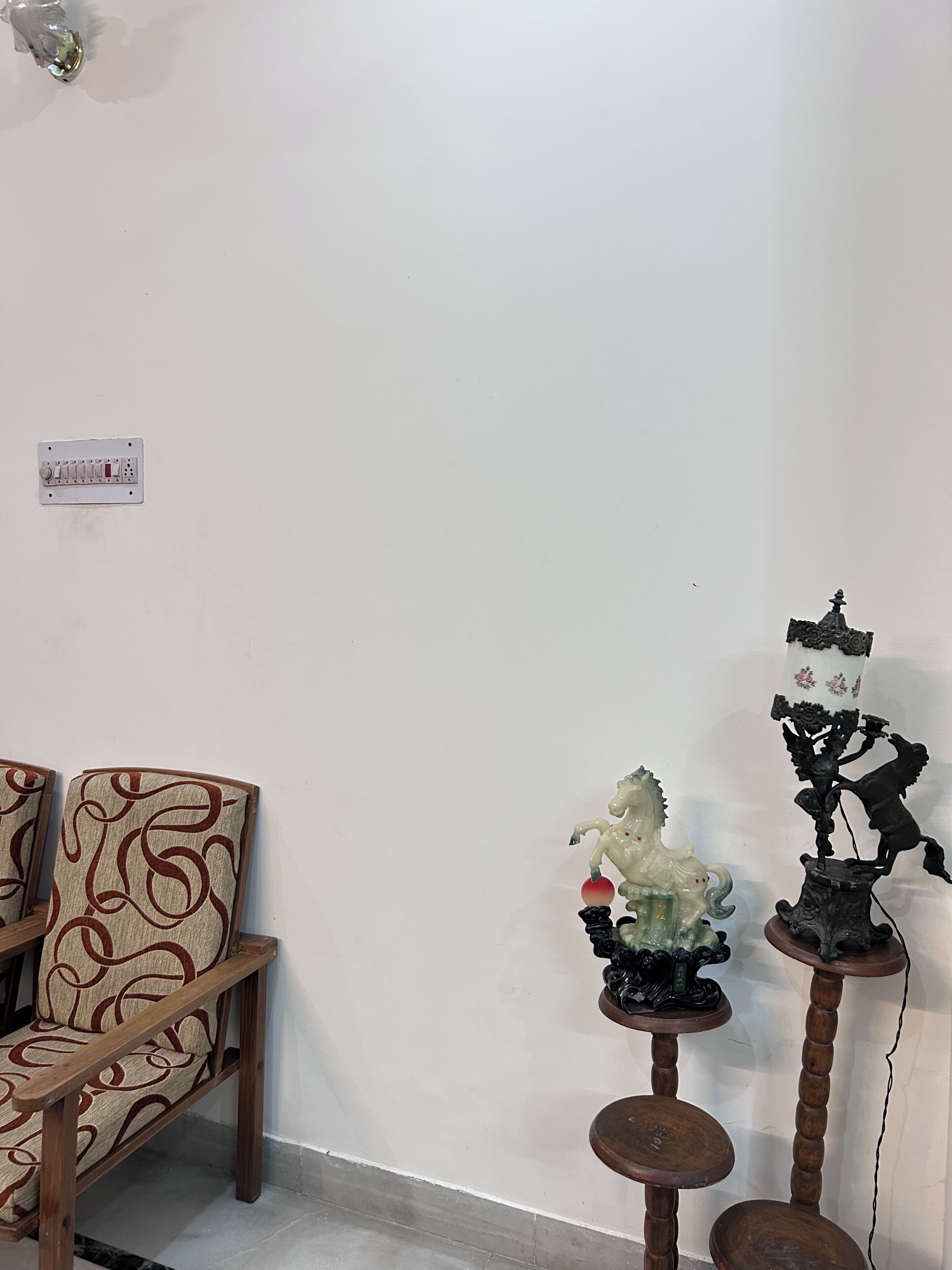 A room with a wooden chair, a small table with a decorative horse figurine, and a wall-mounted electrical outlet.
