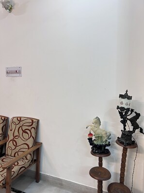 A room with a wooden chair, a small table with a decorative horse figurine, and a wall-mounted electrical outlet. - Charming Bungalow Rental in Jammu (Jammu)