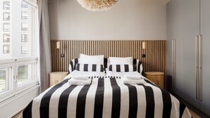 A bedroom with a striped bedspread, wooden headboard, bedside tables, and a hanging light fixture. - Premium 3BR Home | Prime Location | Modern Touch (Helsinki)
