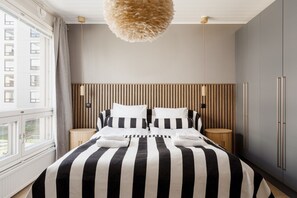 Ein Schlafzimmer mit gestreiftem Bettbezug, einem Holzkopfteil, Nachttischen und einer Pendelleuchte.