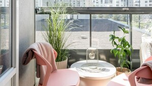 A balcony with two pink chairs, a round table, and a potted plant. - Premium 3BR Home | Prime Location | Modern Touch (Helsinki)