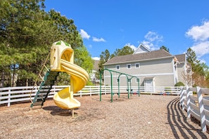 A playground with a yellow spiral slide, surrounded by a white fence and trees.