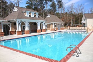 A swimming pool with a covered deck area, a brick building with a gabled roof, and a clear sky.