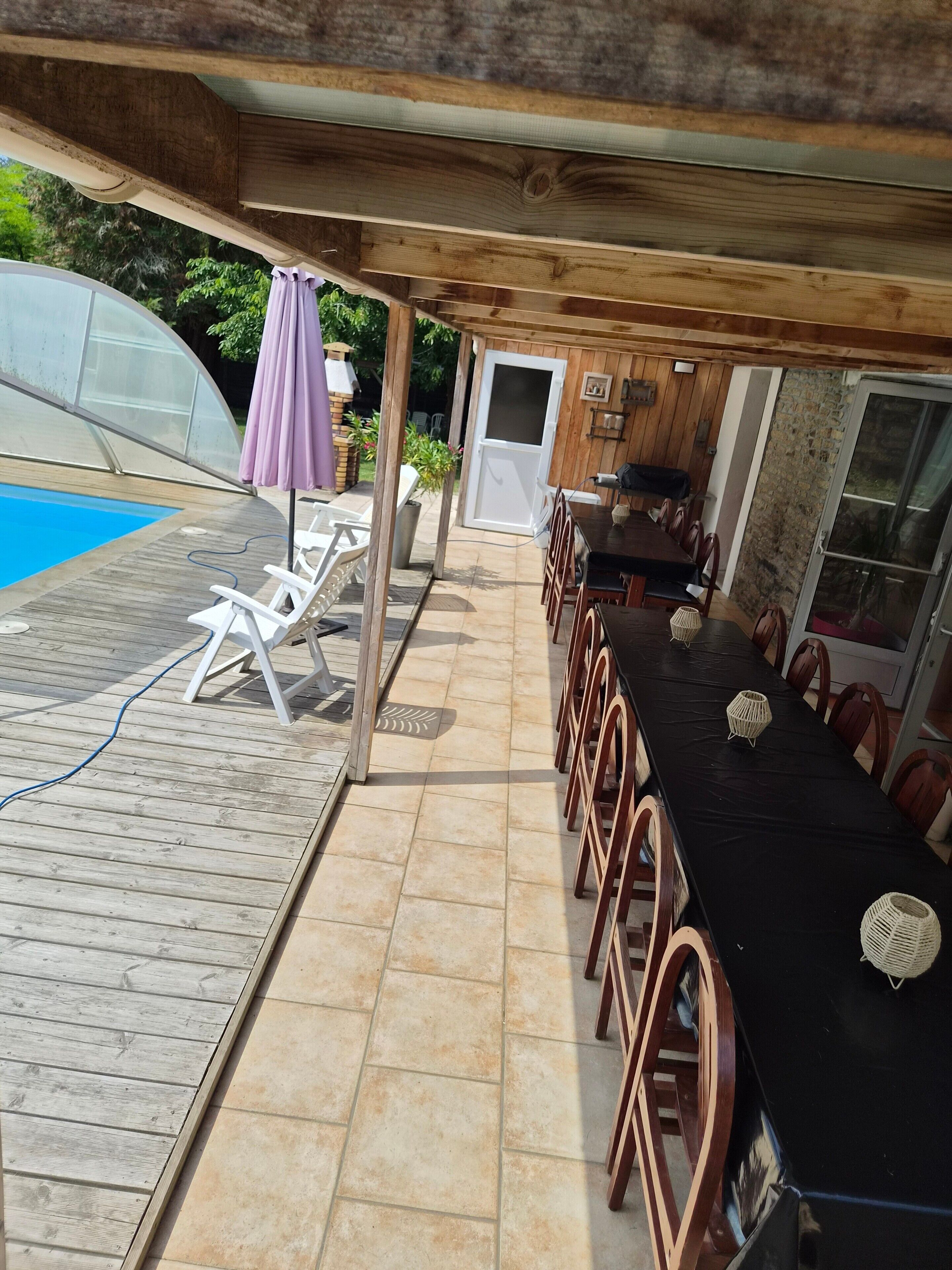 Eine Terrasse im Freien mit Pool, Holzdeck und überdachtem Essbereich mit Stühlen und Tischen.