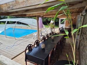 Ein überdachter Außenbereich mit Pool, Esstisch, Stühlen und Sonnenschirmen.
