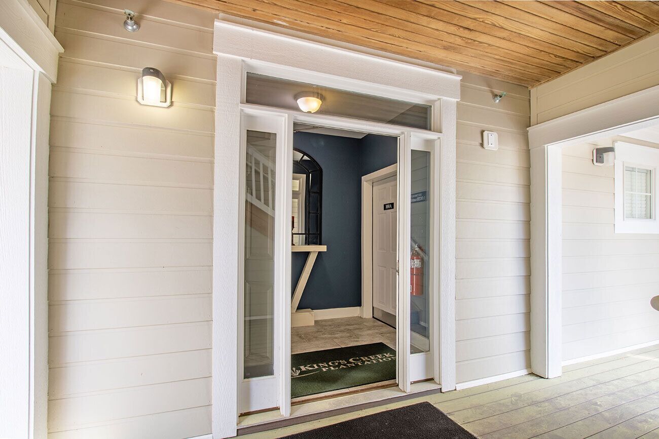 Un couloir avec un plafond en bois, une porte dotée d’un panneau de verre et un paillasson.