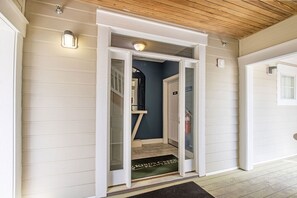Un pasillo con techo de madera, una puerta con panel de vidrio y un felpudo.