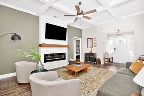 Una sala de estar con chimenea, sofá, mesa de centro y televisor montado en la pared.