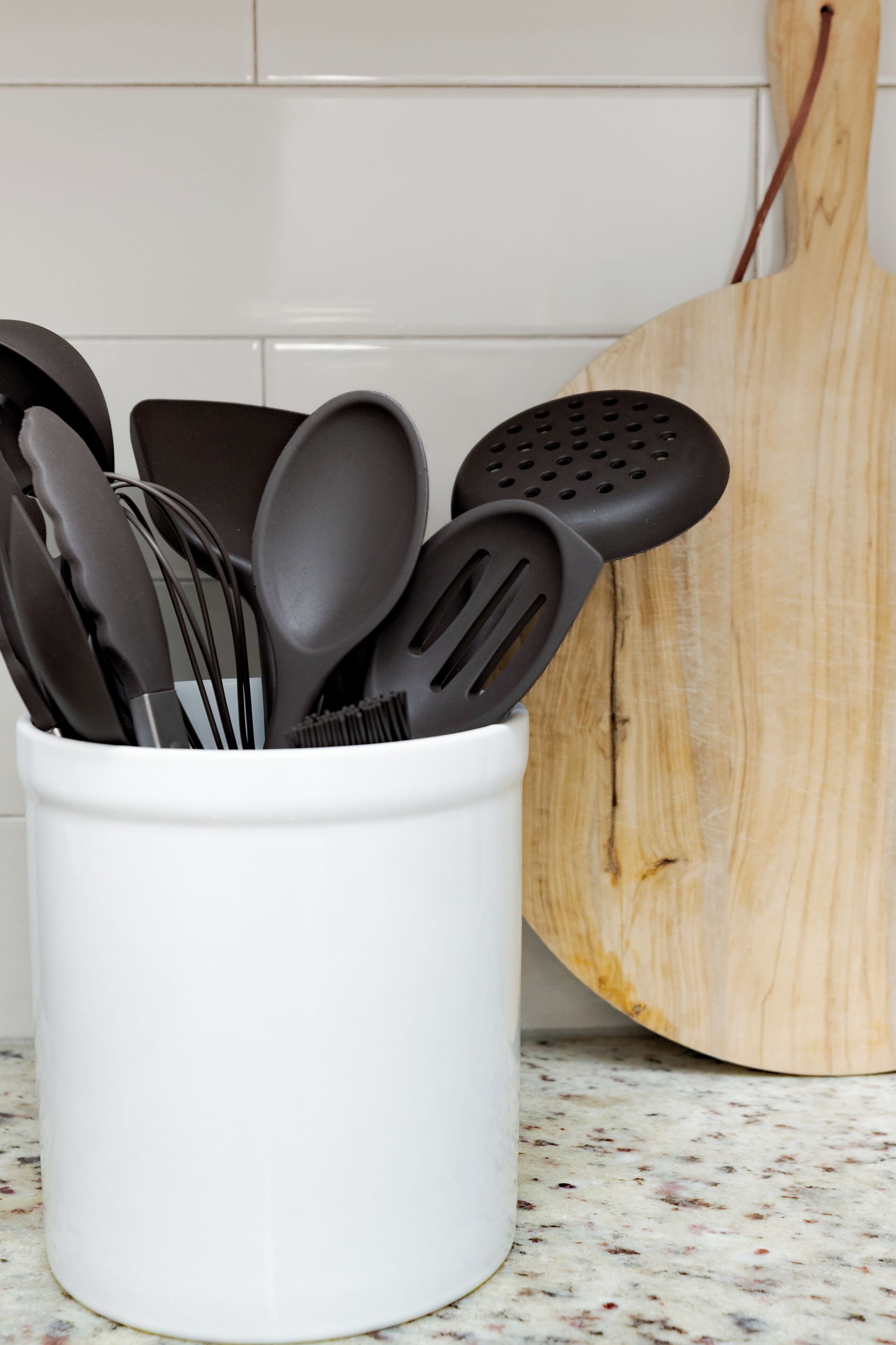 A white utensil holder with black kitchen tools on a kitchen counter.