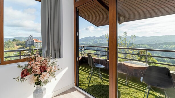 A balcony with a view of mountains, a chair, a table, and a vase with flowers. - Alojamientos Turísticos LA APARECIDA (Ampuero)