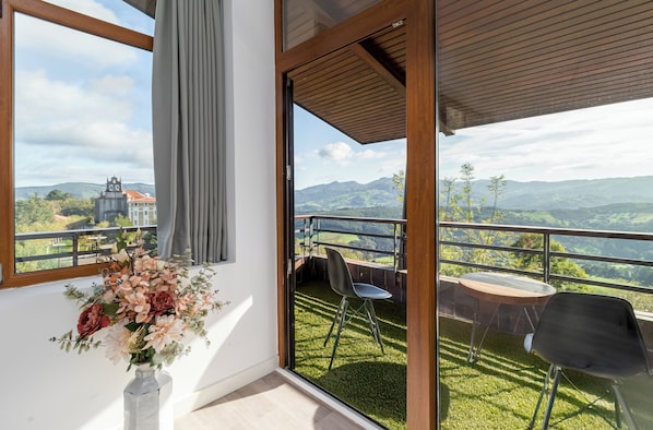Un balcon avec vue sur les montagnes, une chaise, une table et un vase rempli de fleurs.