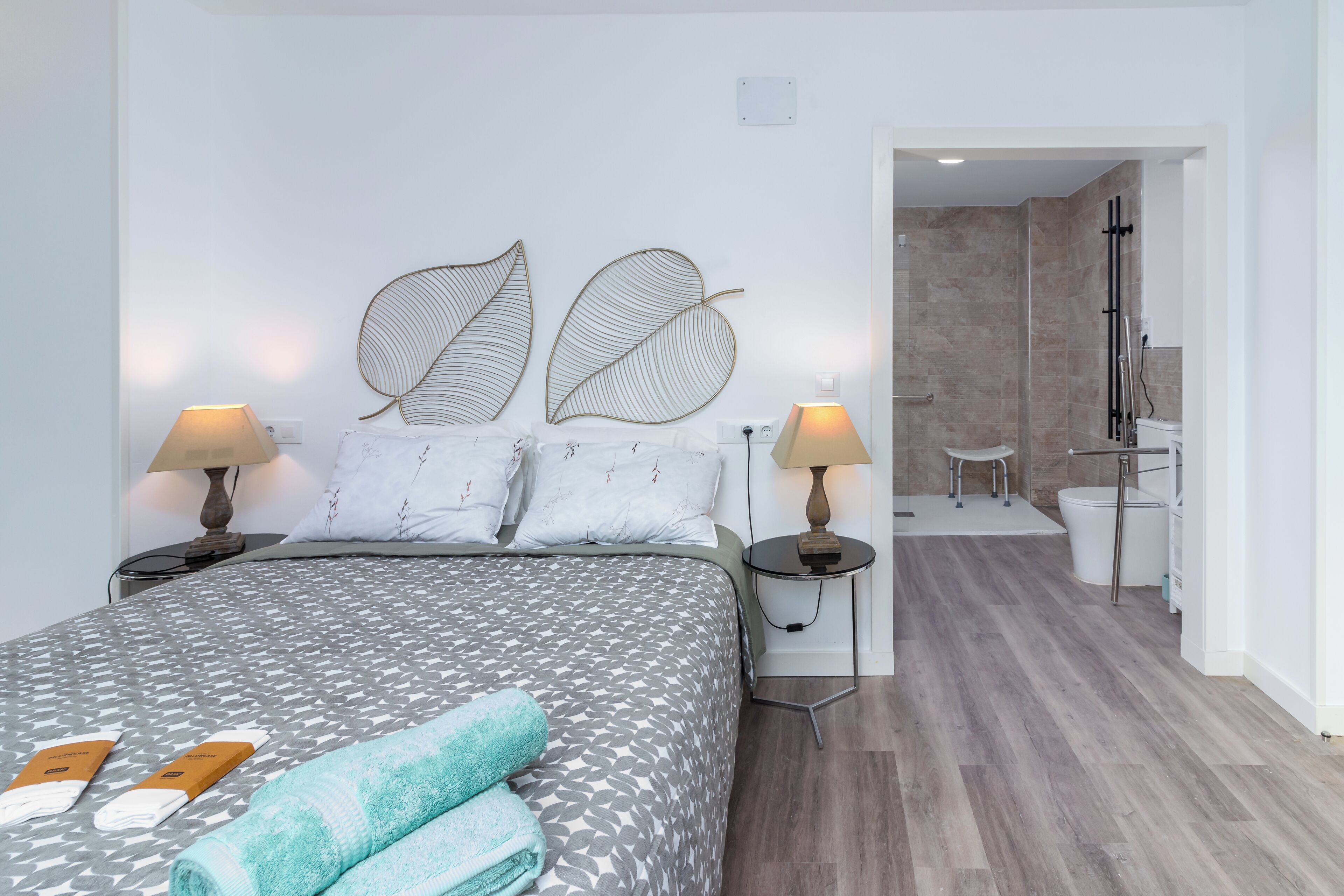 A hotel room with a bed, two nightstands, a bathroom with a shower, and a hallway.
