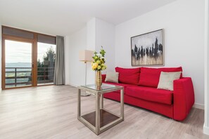 A modern living room with a red sofa, a glass coffee table, and a cityscape painting. - Alojamientos Turísticos LA APARECIDA (AMPUERO)