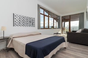 A modern bedroom with a large bed, a sofa, a decorative wall piece, and a view of the outdoors.