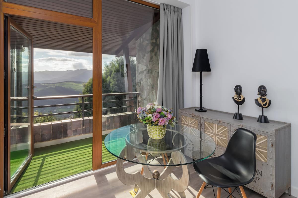 A balcony with a glass table, a chair, a vase of flowers, a lamp, and two decorative items on a cabinet.
