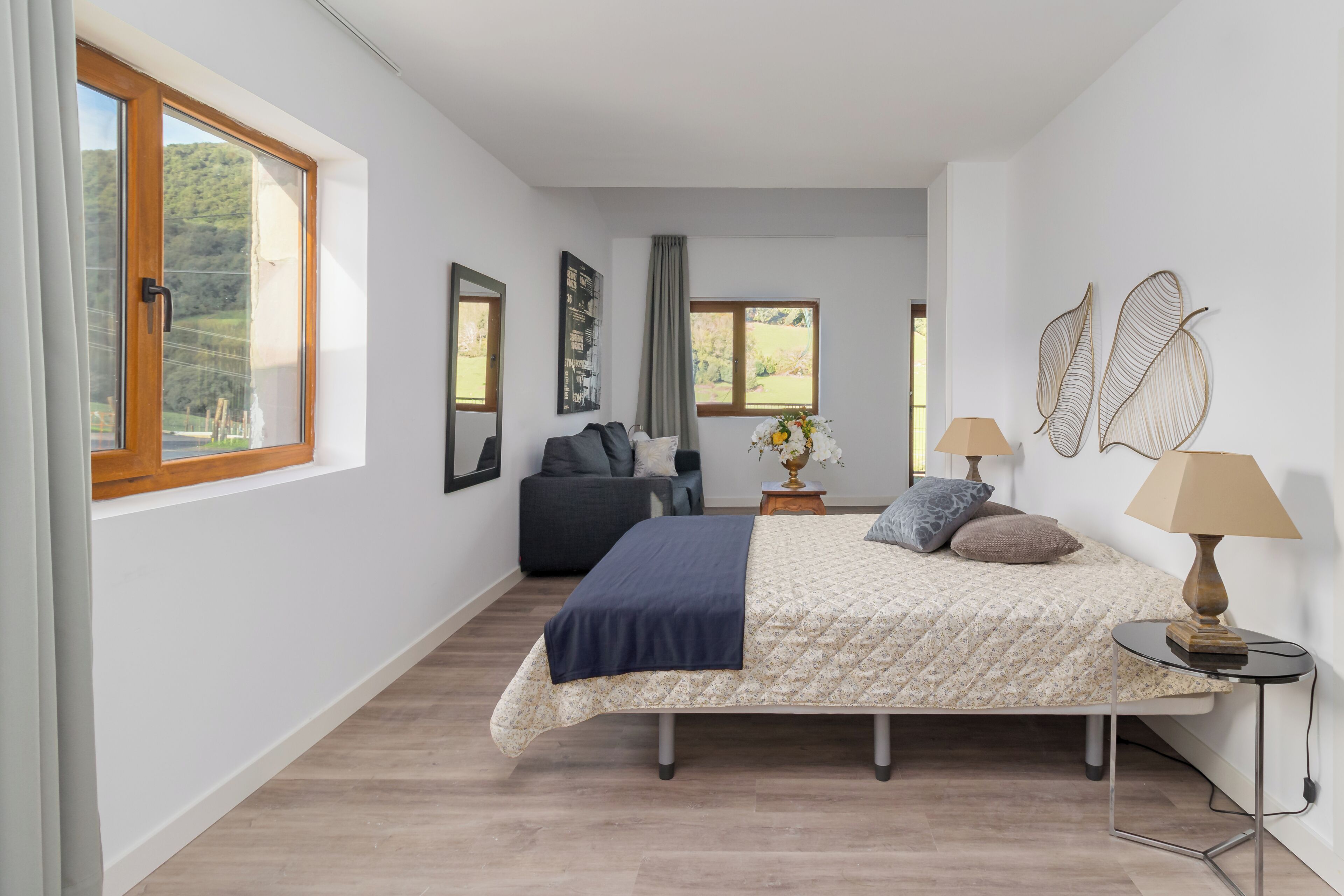A bedroom with a bed, bedside tables, a sofa, and large windows.