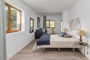 A bedroom with a bed, bedside tables, a sofa, and large windows. - Alojamientos Turísticos LA APARECIDA (AMPUERO)