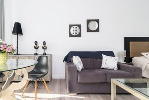 Una sala de estar moderna con una mesa de vidrio, un sofá, una lámpara y elementos decorativos en la pared.