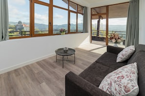 A modern living room with a sofa, a small round table, and a view of mountains and a church through large windows.