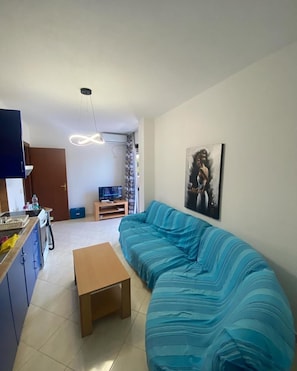 En stue med sofa, sofabord, fjernsyn og et billede på væggen.