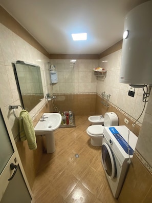 Un baño con lavamanos, dos inodoros, lavadora, espejo y ducha.
