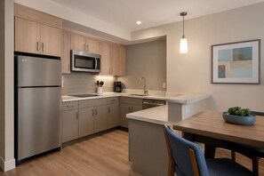 A modern kitchen with stainless steel appliances, wooden cabinets, a white countertop, and a pendant light. - The Avelyn Suites (Toronto)