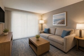 A hotel room with a sofa, two lamps, a TV, a framed picture, and a plant. - The Avelyn Suites (Toronto)