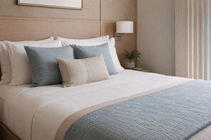A neatly made bed with a white and blue bedspread, a bedside lamp, and a vase with a plant on a wooden nightstand. - The Avelyn Suites (Toronto)