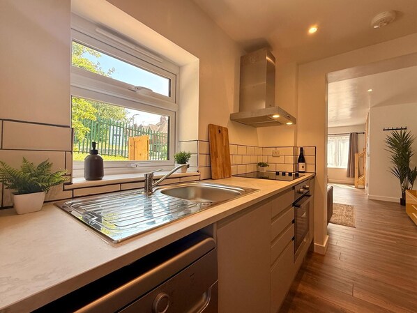 A modern kitchen with a window, stainless steel sink, wooden countertop, and built-in oven. - Unique Devon Cottages - Sunrise Cottage - Stylish & Comfortable (Exmouth)
