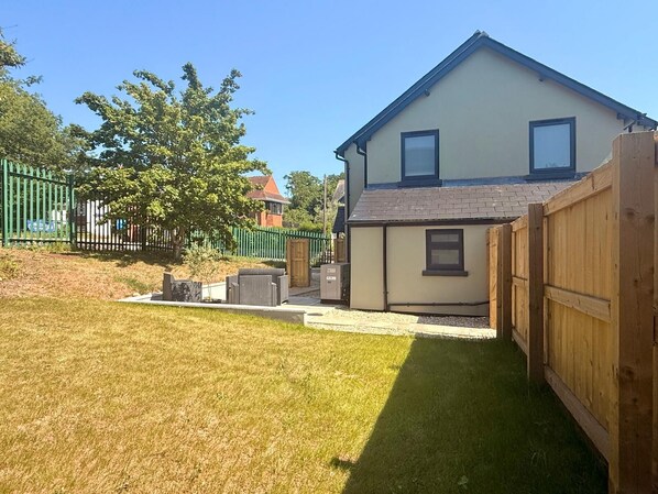A two-story house with a small front yard, a wooden fence, and a green fence in the background. - Unique Devon Cottages - Sunrise Cottage - Stylish & Comfortable (Exmouth)