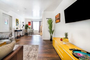 A modern living room with a sofa, a coffee table, a TV mounted on the wall, and a fruit bowl on a yellow cabinet. - Unique Devon Cottages - Sunrise Cottage - Stylish & Comfortable (Exmouth)
