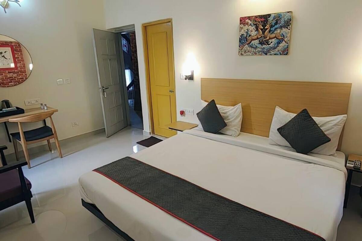 Habitación de hotel con cama, mesitas de noche, escritorio, silla, armario y puerta que da a otra habitación.