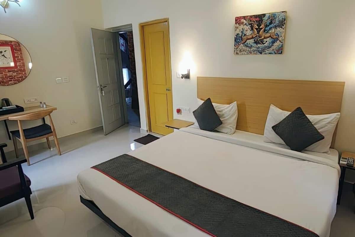Habitación de hotel con cama, mesitas de noche, escritorio, silla, armario y puerta que da a otra habitación.