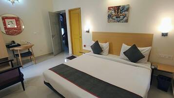 Habitación de hotel con cama, mesitas de noche, escritorio, silla, armario y puerta que da a otra habitación.