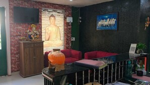 A room with a Buddha statue, a TV, a painting, and a red sofa. - Hotel Menkaa (Patna)
