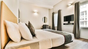 A modern hotel room with a large bed, a flat-screen TV, a bedside table, and a window with curtains. - Hotel Menkaa (Patna)