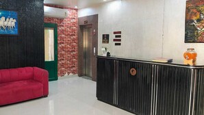 A reception area with a red sofa, a black reception desk, a painting of horses, a brick wall, and a lift. - Hotel Menkaa (Patna)